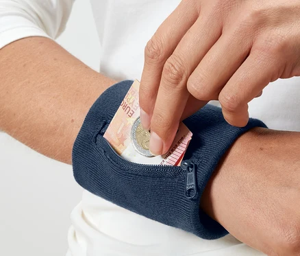 Ruka vkládá euro bankovku a minci do modré bezpečnostní peněženky na zápěstí.