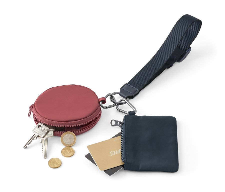 Vínová kulatá peněženka s klíči a mincemi vedle modré peněženky na zip s kartami a multifunkční klíčenkou.