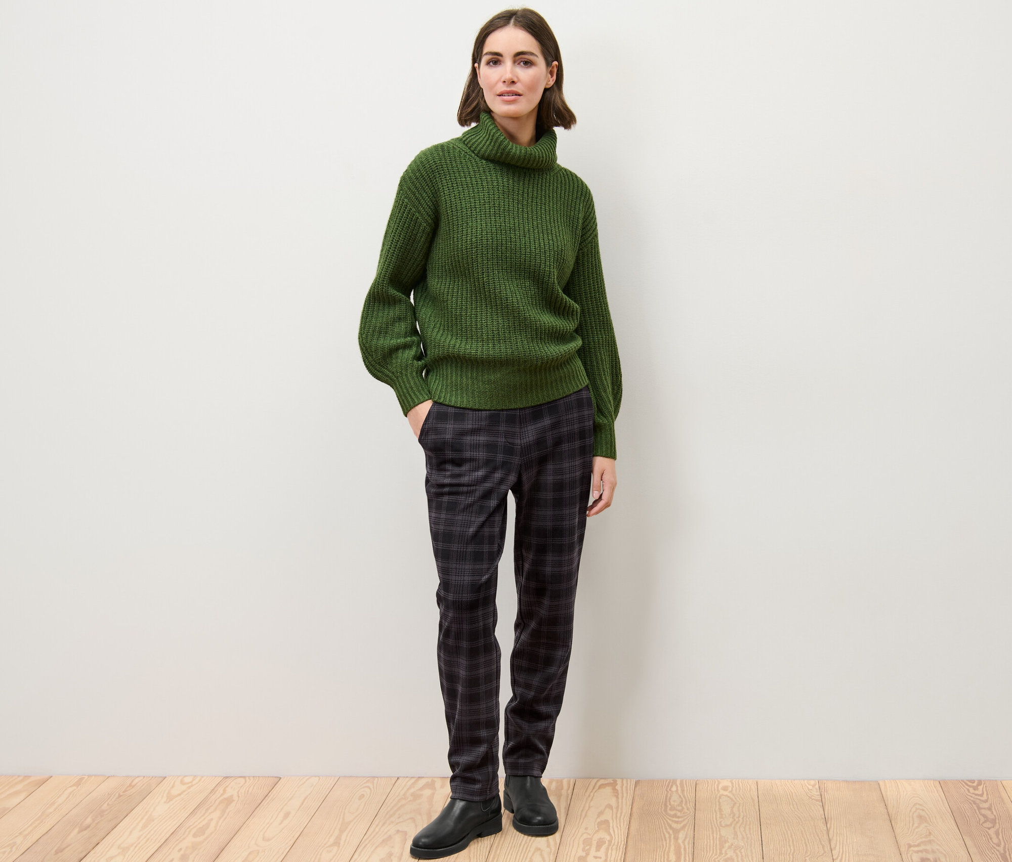 Žena stojí a pózuje v zeleném svetru a kostkovaných kalhotách joggpant.