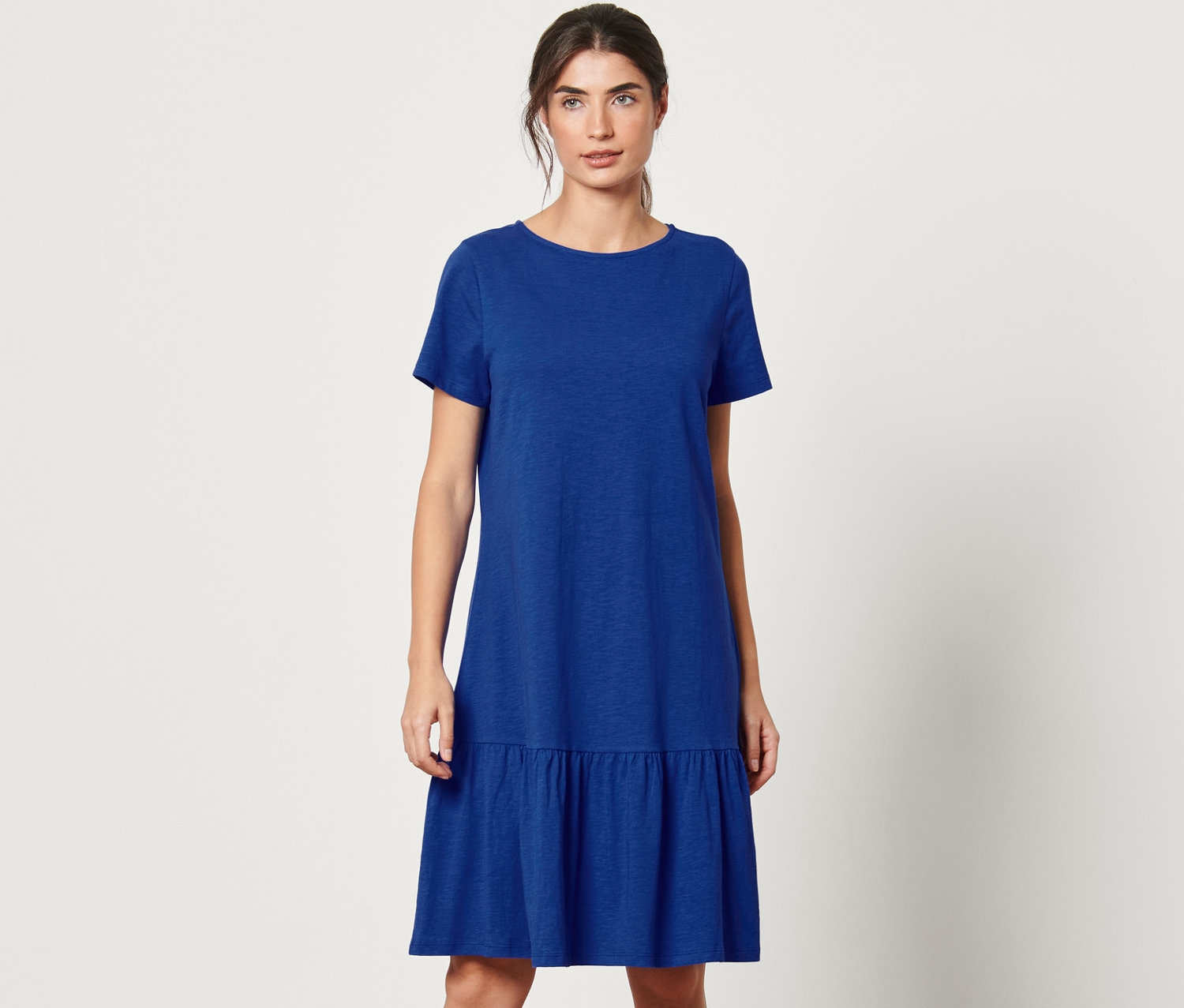 Žena stojí a pózuje v kobaltově modrých žerzejových šatech s volánem.