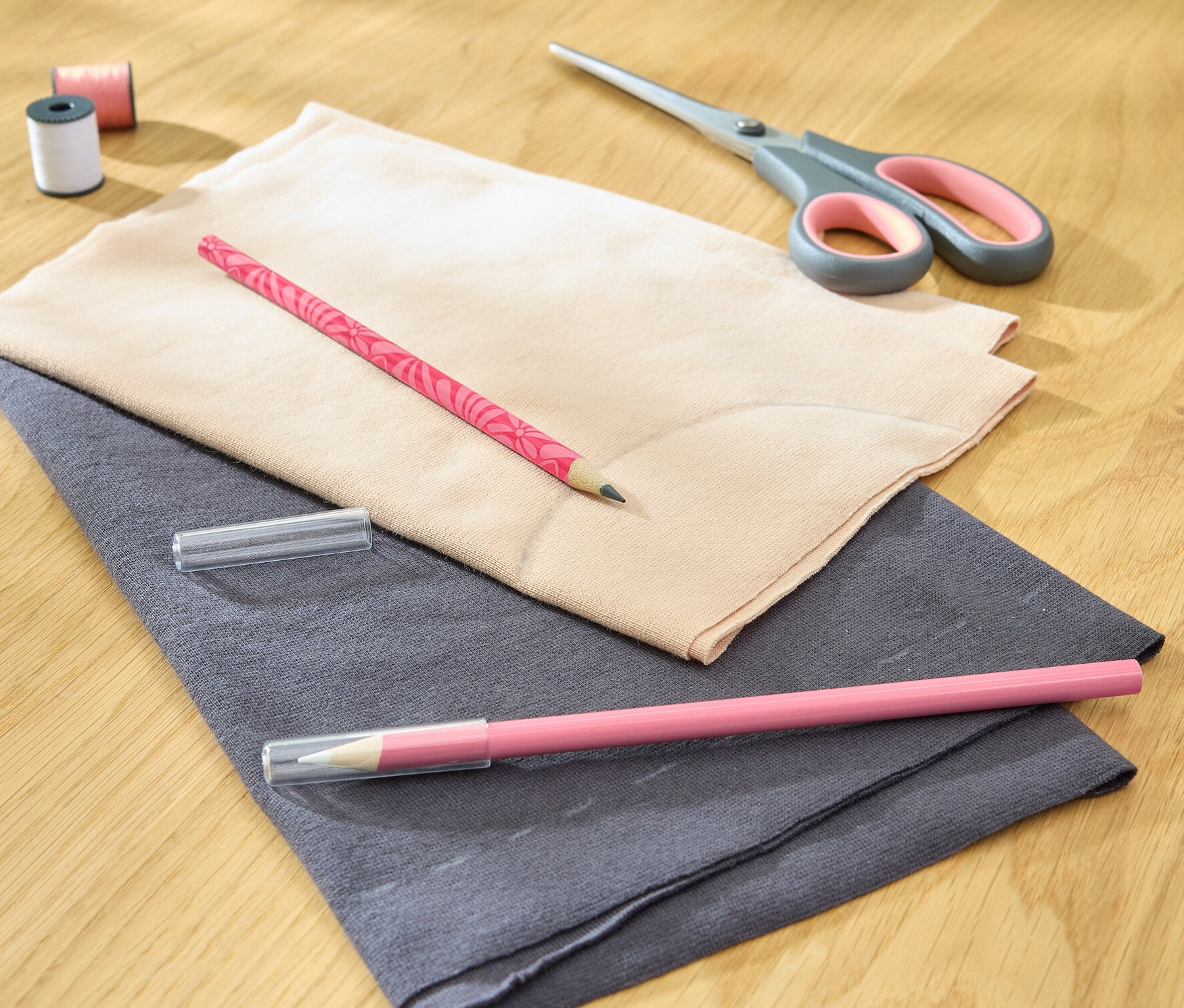 Dva látkové křídové popisovače leží na látce s nůžkami, nití a cívkou.