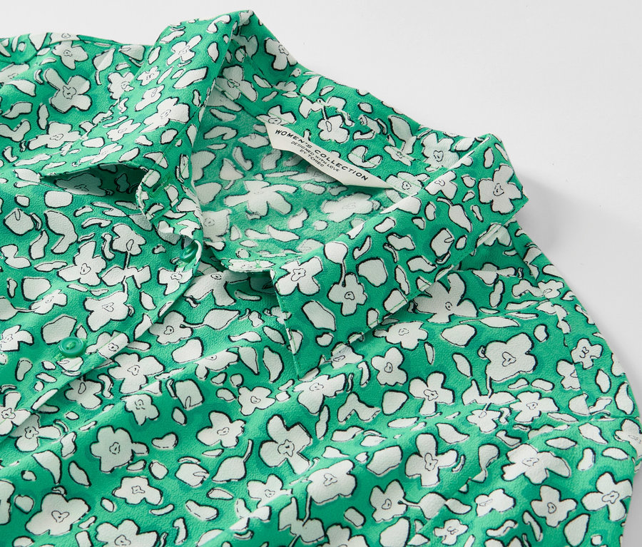 Detail zelených košilových šatů s bílým potiskem květin.