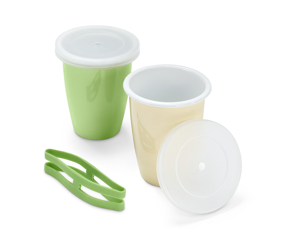 Dva piknikové kelímky s víčky, jeden zelený a jeden krémový, a zelený držák na kelímky.