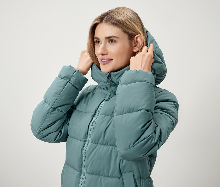 Žena si upravuje kapuci na modrozelené péřové bundě.