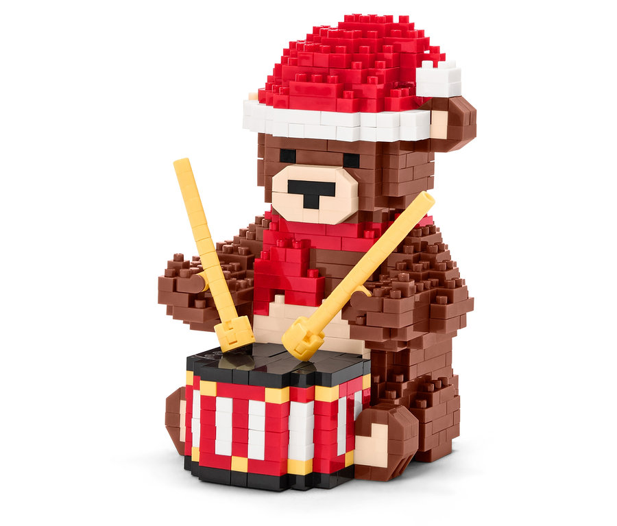 Hnědý medvídek z kostek s červenou čepicí a šálou hraje na buben s paličkami.