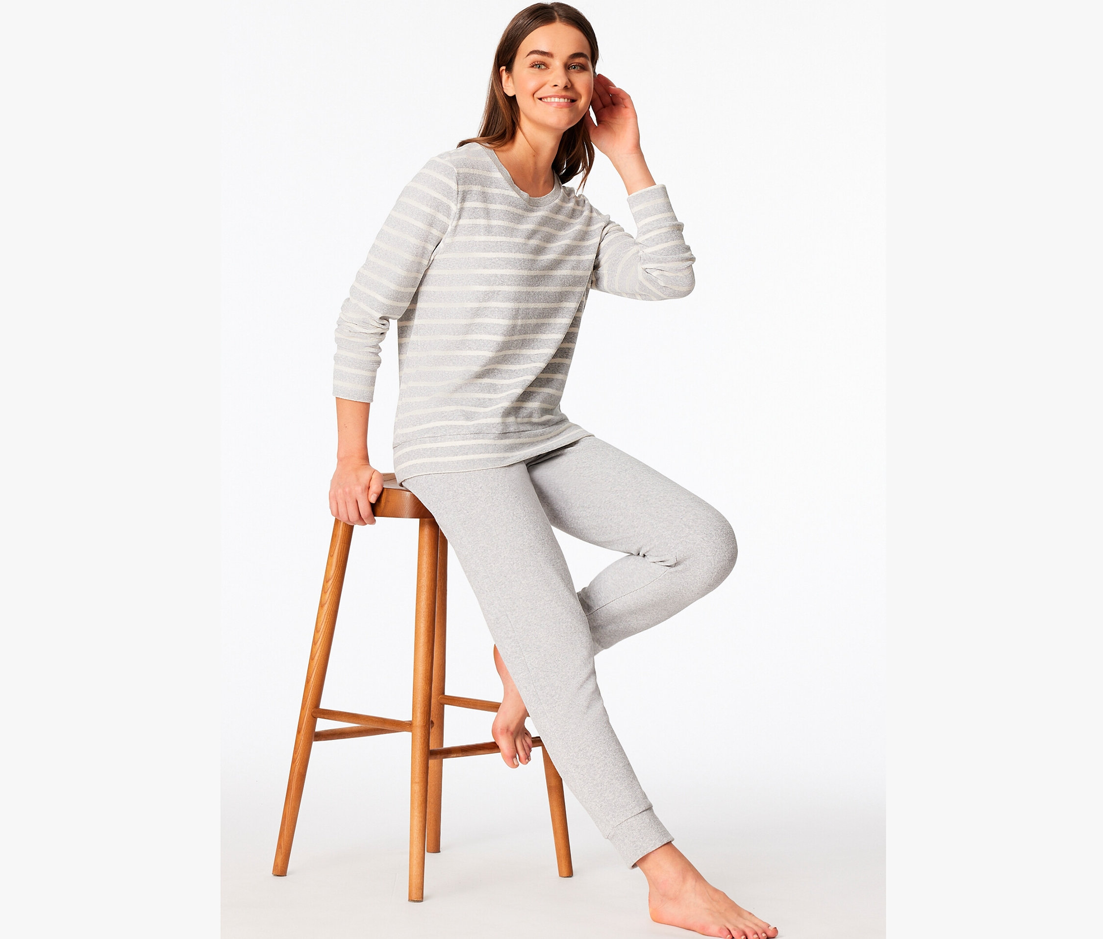 Žena sedí na dřevěné stoličce a má na sobě šedé pruhované pyžamo.