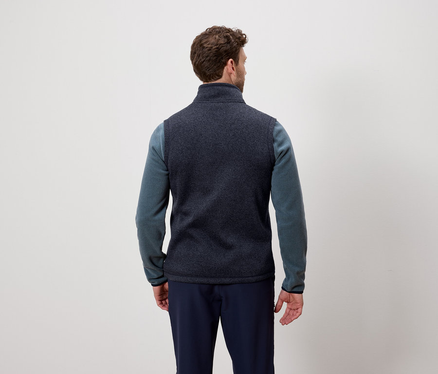 Muž zády k fotoaparátu má na sobě tmavě modrou vestu a modrý svetr.