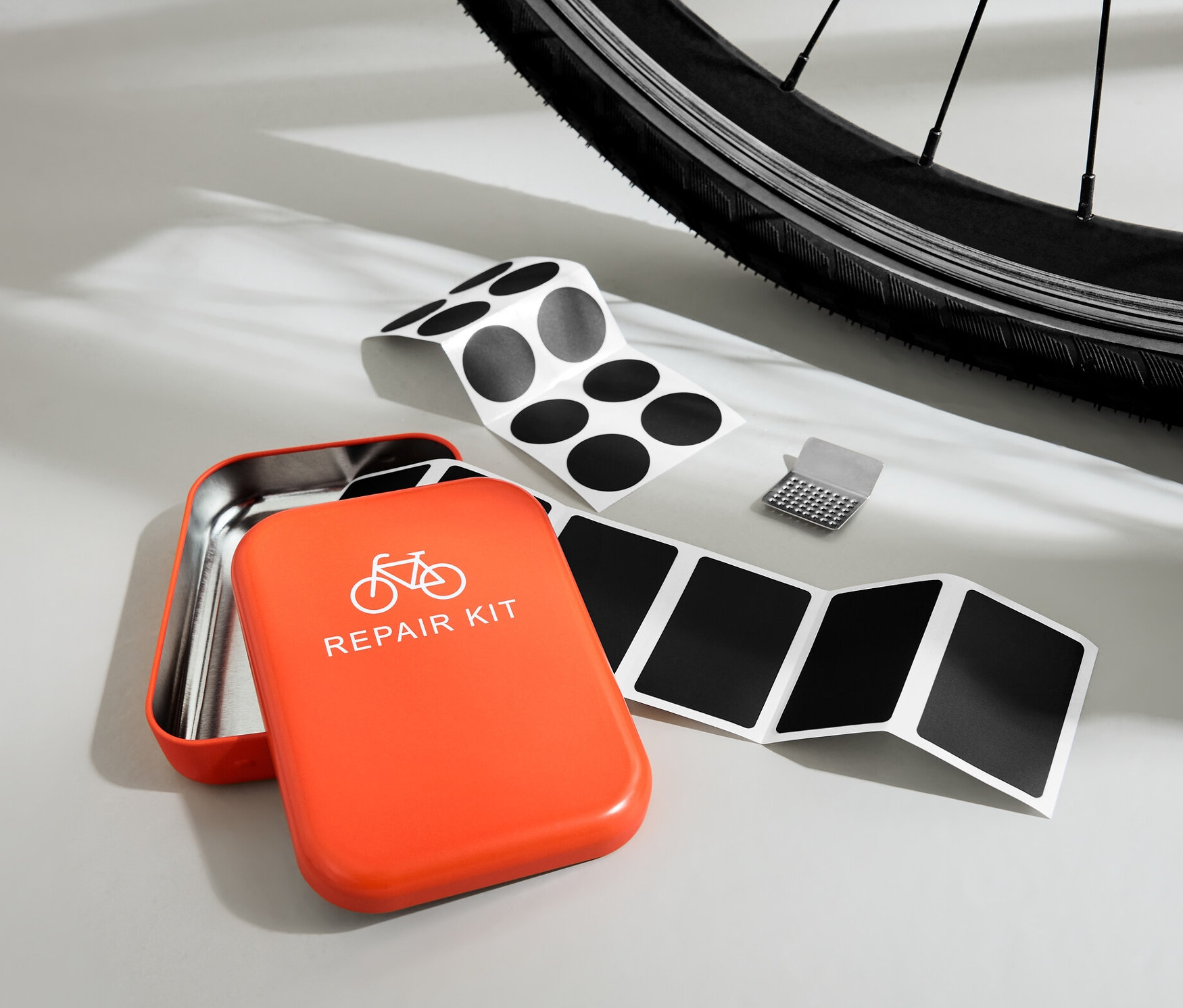 Otevřená oranžová sada na opravu jízdních kol s náplastmi a struhadlem na pozadí kola.