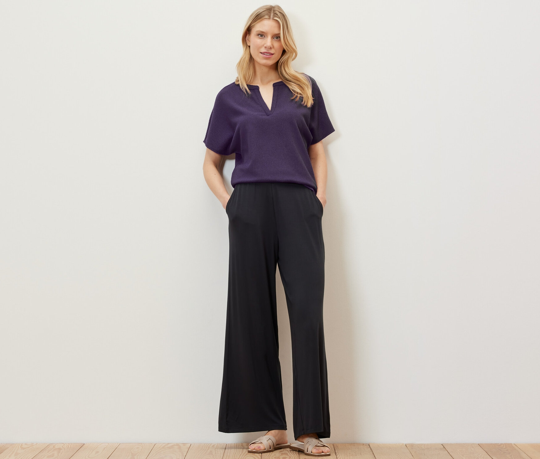 Blondýna pózuje ve strukturované halence s krátkým rukávem a černých kalhotách.