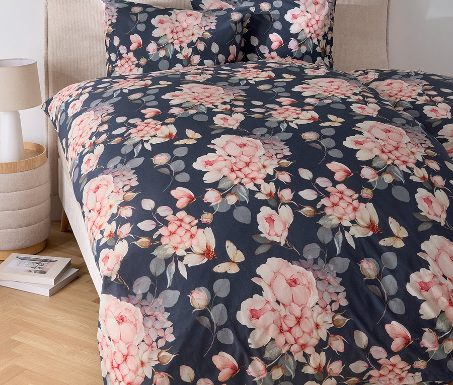 Postel s květinovým ložním prádlem a nočním stolkem s lampou.