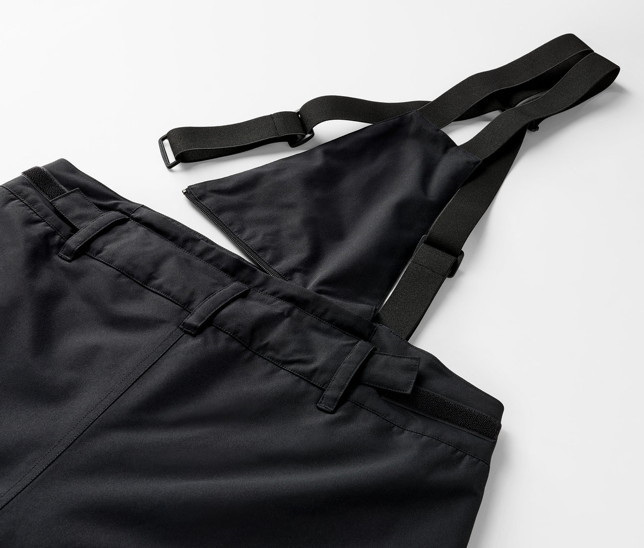 Detail černých kalhot s laclem a elastickými popruhy.