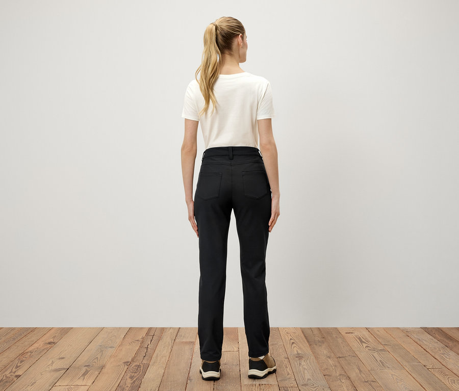 Zezadu je vidět žena s blond vlasy v culíku, která má na sobě bílé tričko a černé kalhoty.