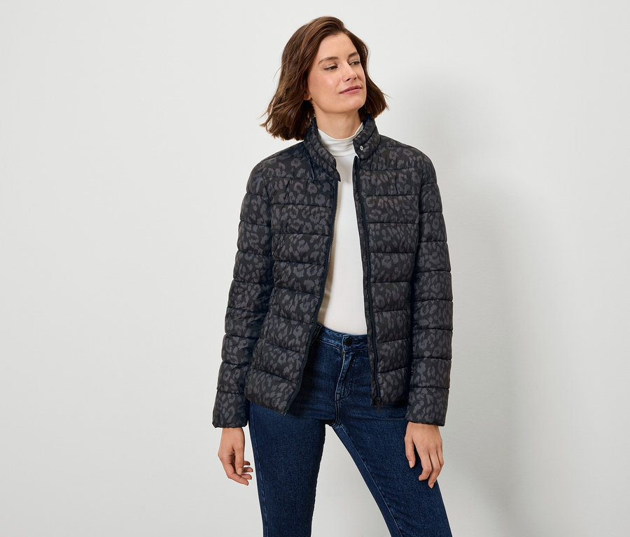Žena má na sobě černou péřovou bundu s potiskem a džíny.