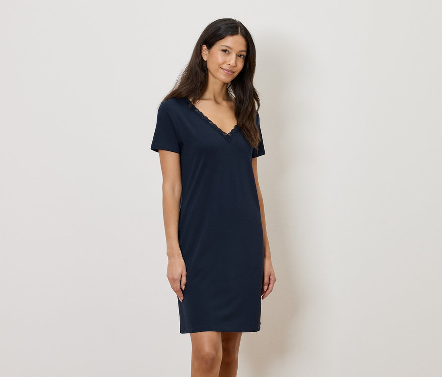 Žena má na sobě tmavě modré šaty ke kolenům s krajkovým lemem na výstřihu do V.