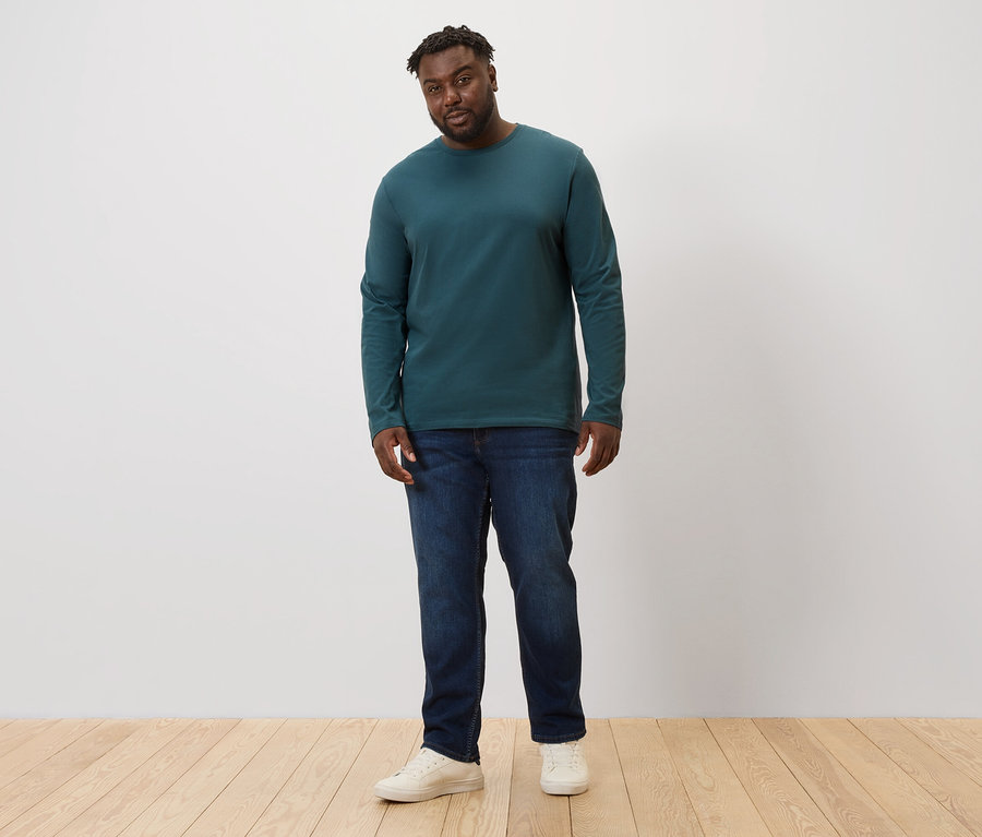 Muž stojí a má na sobě džíny a zelené tričko s dlouhým rukávem, 2 ks.