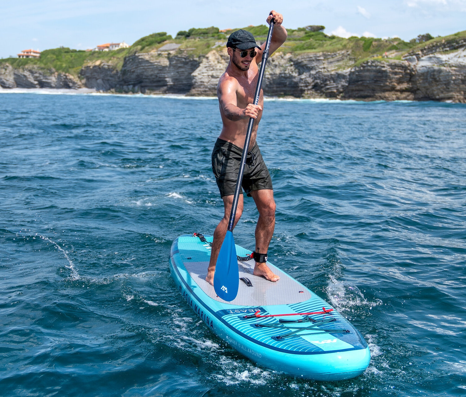 Muž pádluje na modrém paddleboardu Aqua Marina »Beast« 10'6“ na moři.