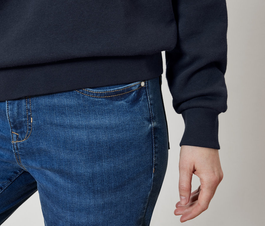 Detail modrých džínů a tmavě modré mikiny na těle osoby.