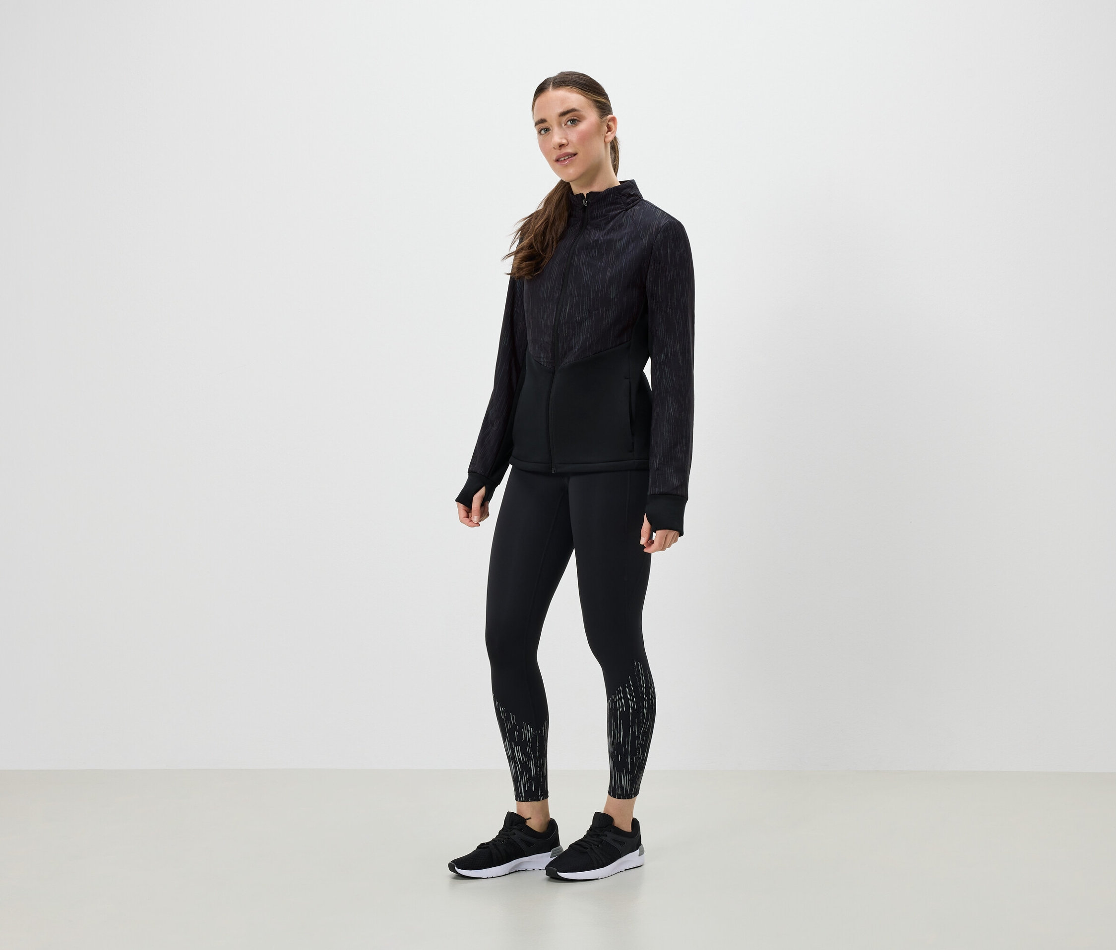 Žena v černém sportovním oblečení pózuje na světlém pozadí.