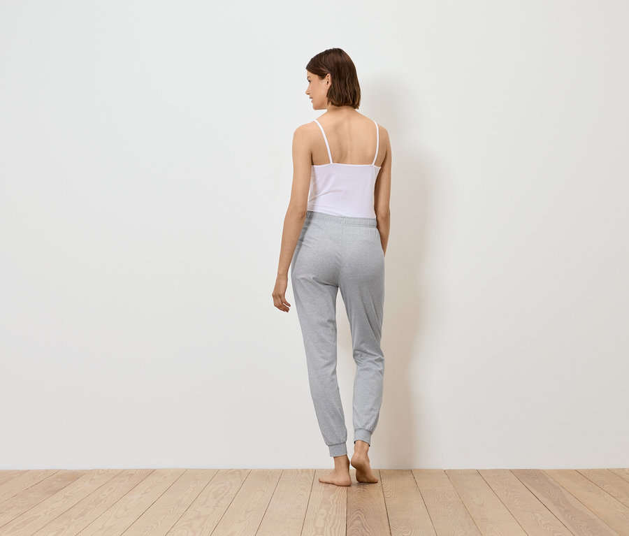 Žena stojí zády, má na sobě bílý top a šedé tepláky.