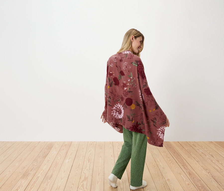 Žena se dívá přes rameno a pózuje v květovaném přehozu a zelených kalhotách.