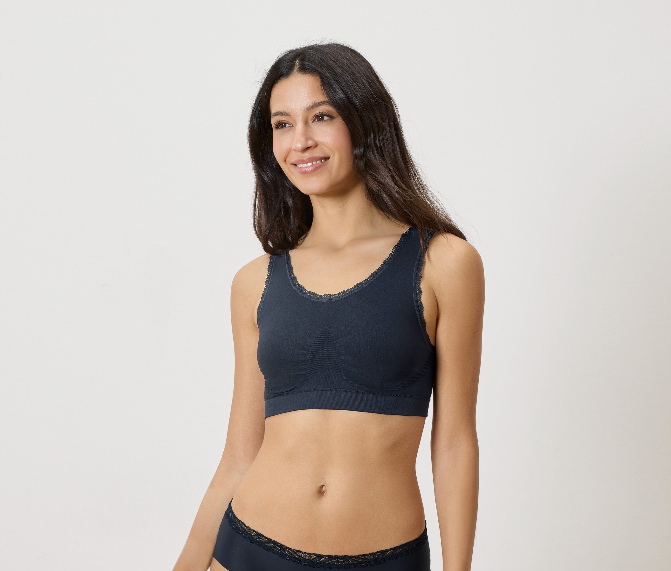 Žena má na sobě tmavě modrou podprsenku s krajkovým lemem a odpovídající spodní prádlo.