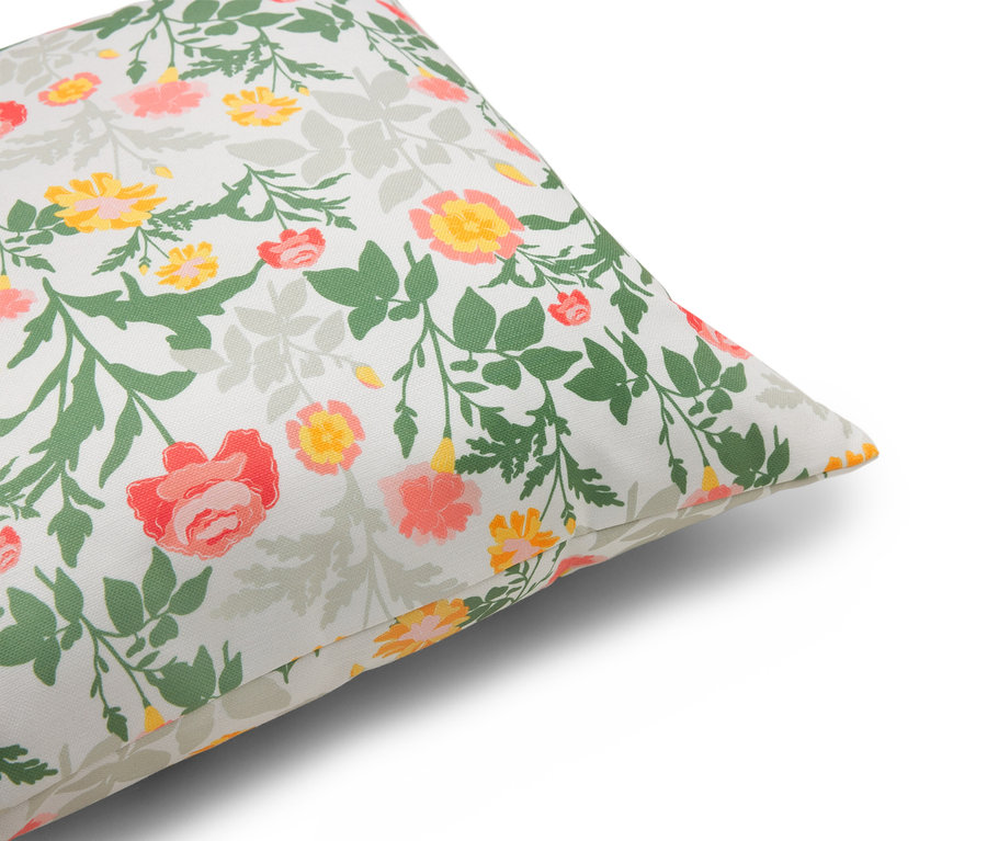 Detailní záběr polštáře s květinovým vzorem v červených, žlutých a zelených tónech na bílém pozadí.