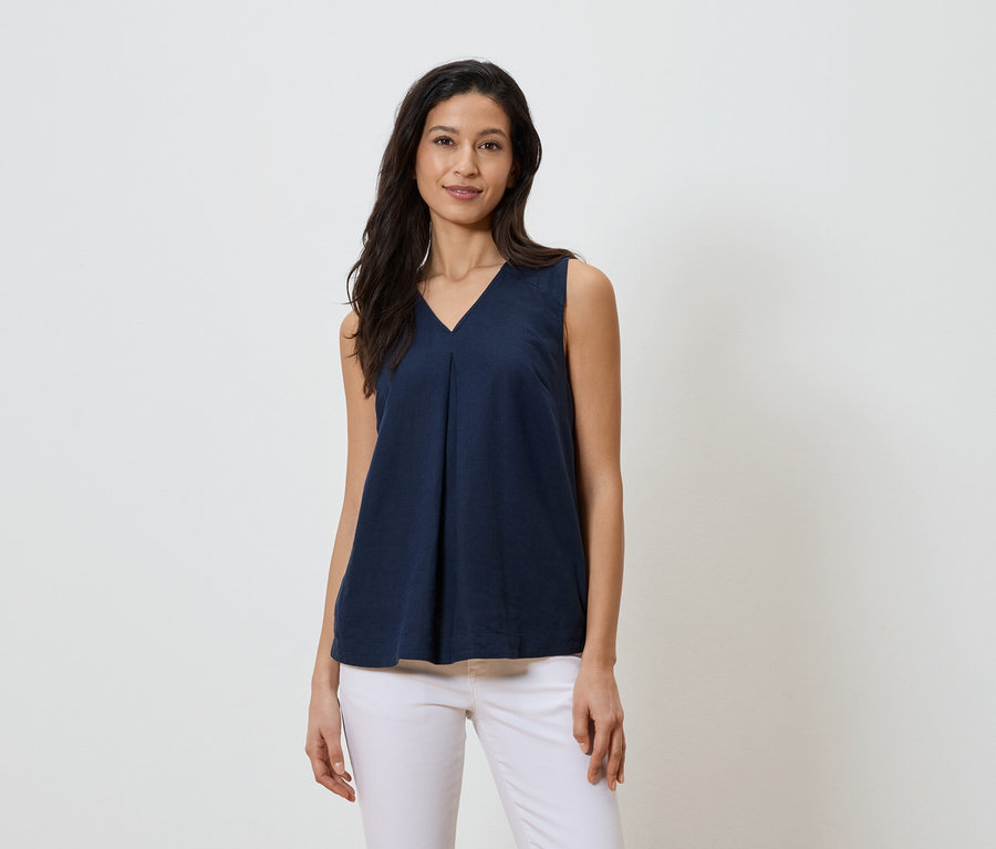 Žena má na sobě tmavě modrý top bez rukávů s výstřihem do V a bílé džíny.