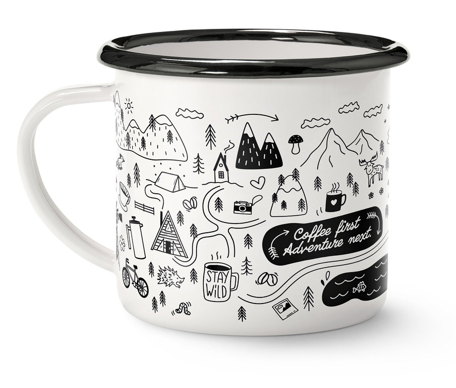 Bílý hrnek s černým okrajem a uchem, zdobený kresbou hor, stromů a nápisem "Coffee first, Adventure next".