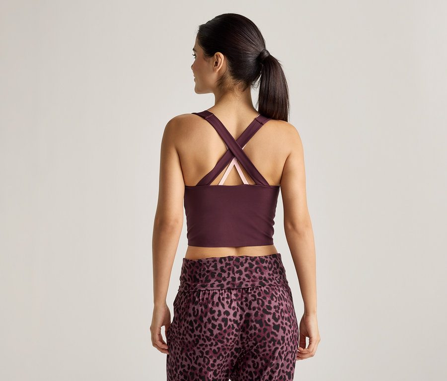 Pohled zezadu na ženu s culíkem, která má na sobě vínový crop top se zkříženými ramínky a kalhoty s leopardím vzorem.