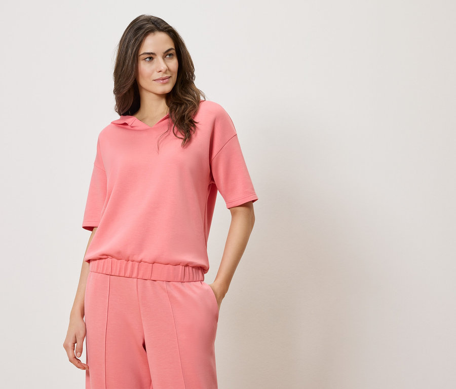 Žena má na sobě růžovou mikinu s krátkým rukávem a kapucí a růžové kalhoty.