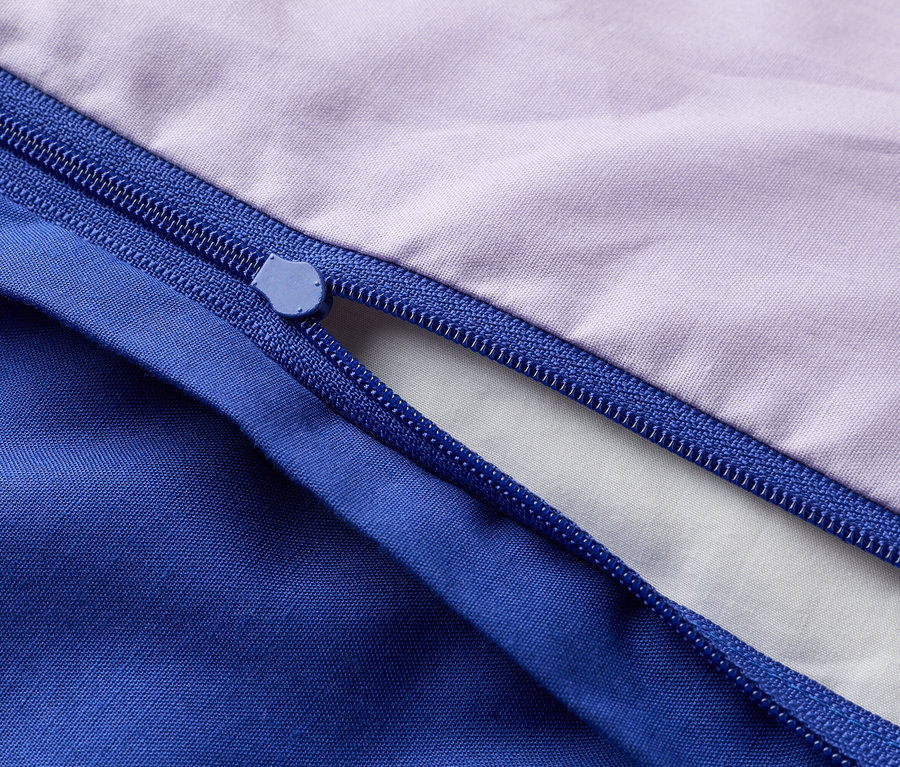 Detailní záběr na částečně otevřený zip na fialové a modré látce.