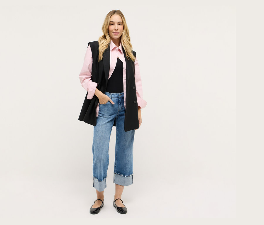 Žena v černé vestě, růžové košili, džínách a černých botách.