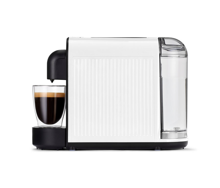 Bílý kávovar Cafissimo now white se sklenicí plnou kávy stojí na stole.
