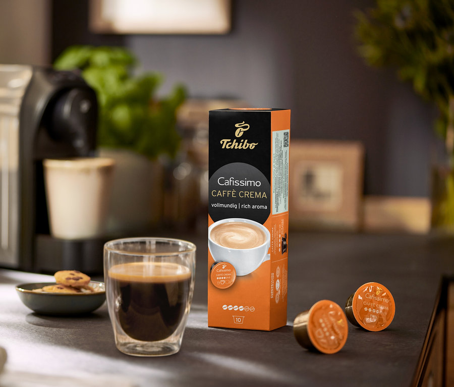 Kávovar s šálkem kávy, sušenkami a balením kapslí Cafissimo Caffe Crema.