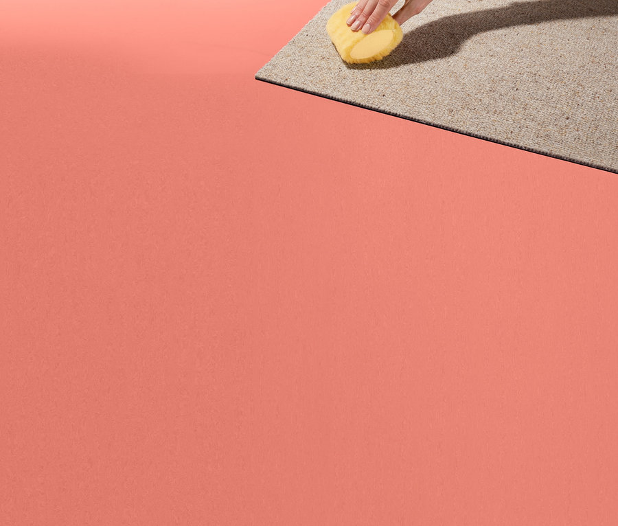 Ruka drží houbičku na skvrny a čistí koberec.