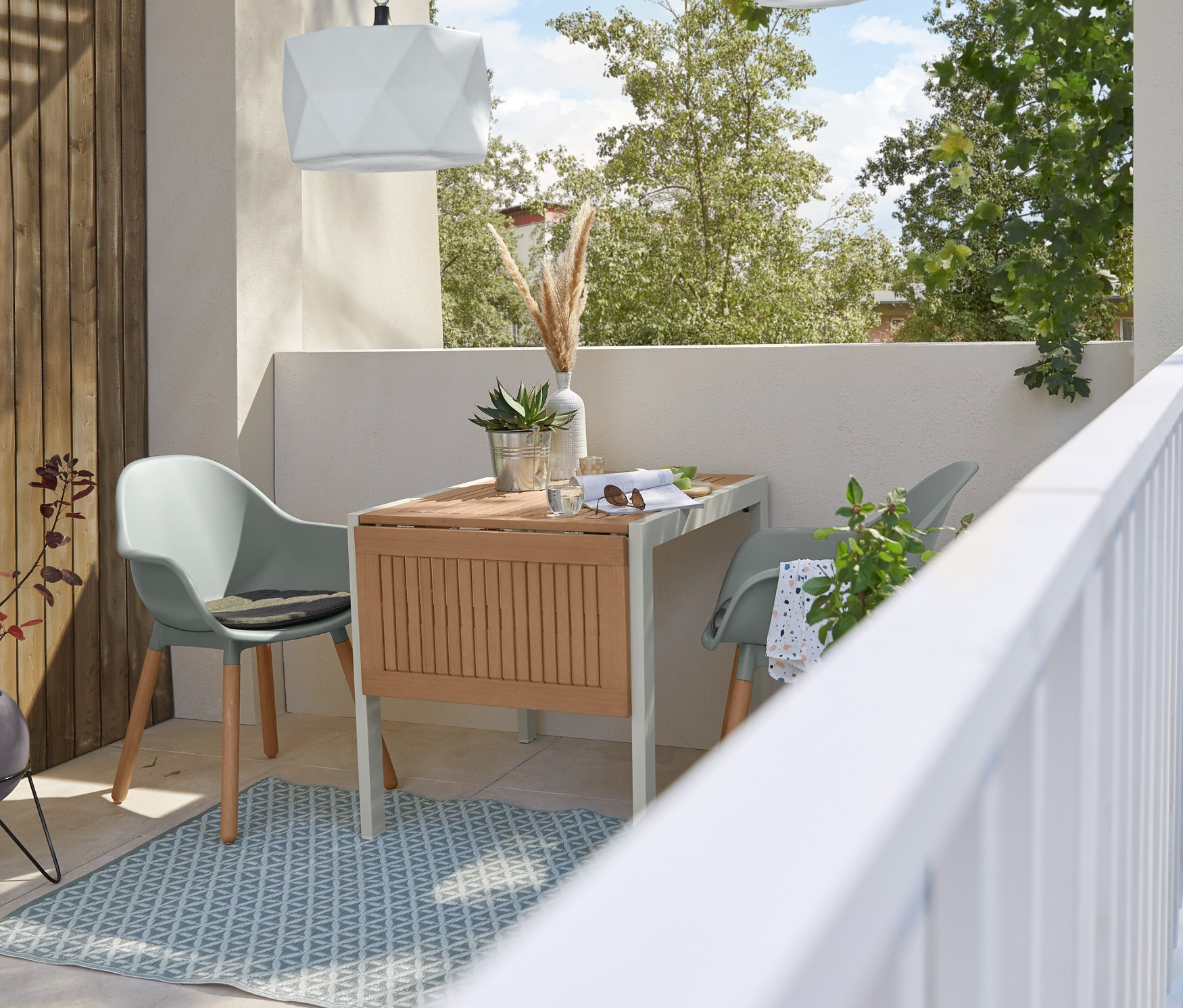 Dvě šedé zahradní židle stojí u rozkládacího stolu na venkovním koberci pod závěsným LED svítidlem.