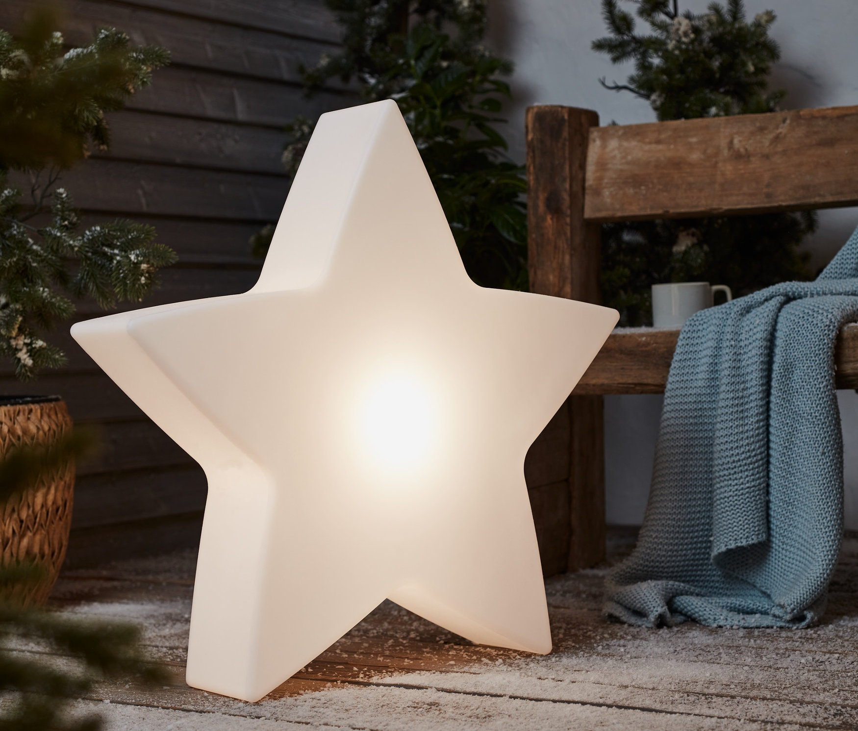 Velké solární zahradní světlo Hvězda stojí na zasněžené dřevěné terase vedle lavice.
