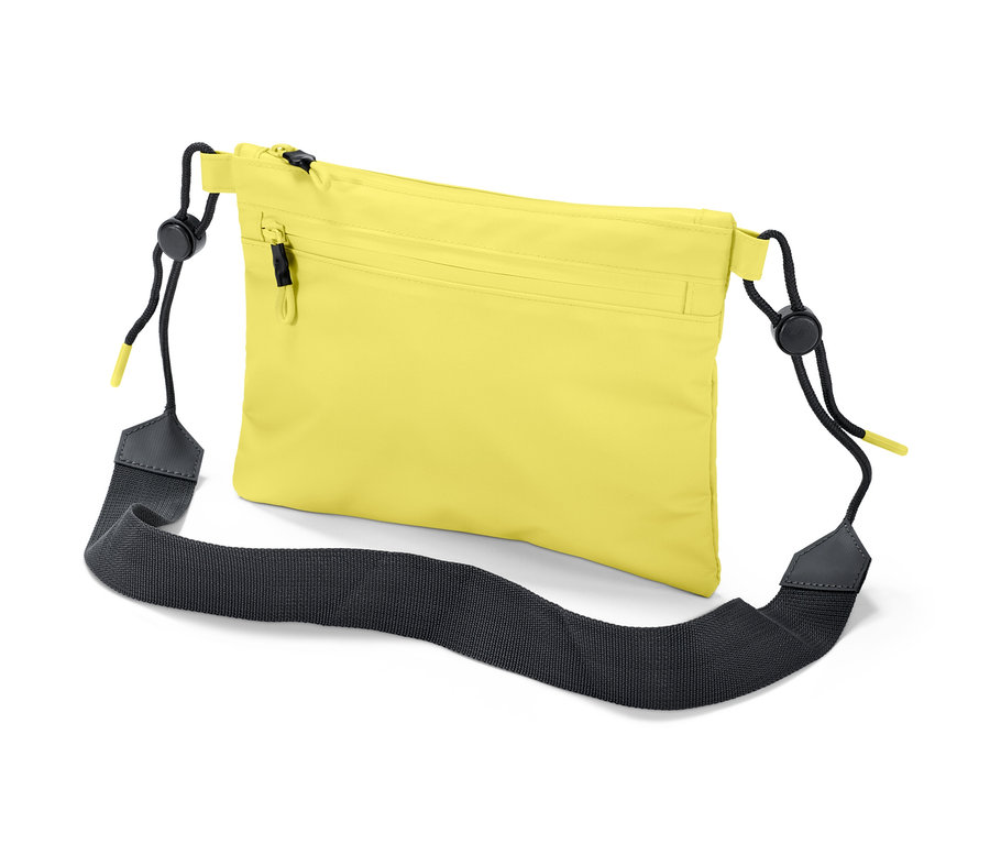 Žlutá taška přes rameno s černým popruhem leží na bílém pozadí.