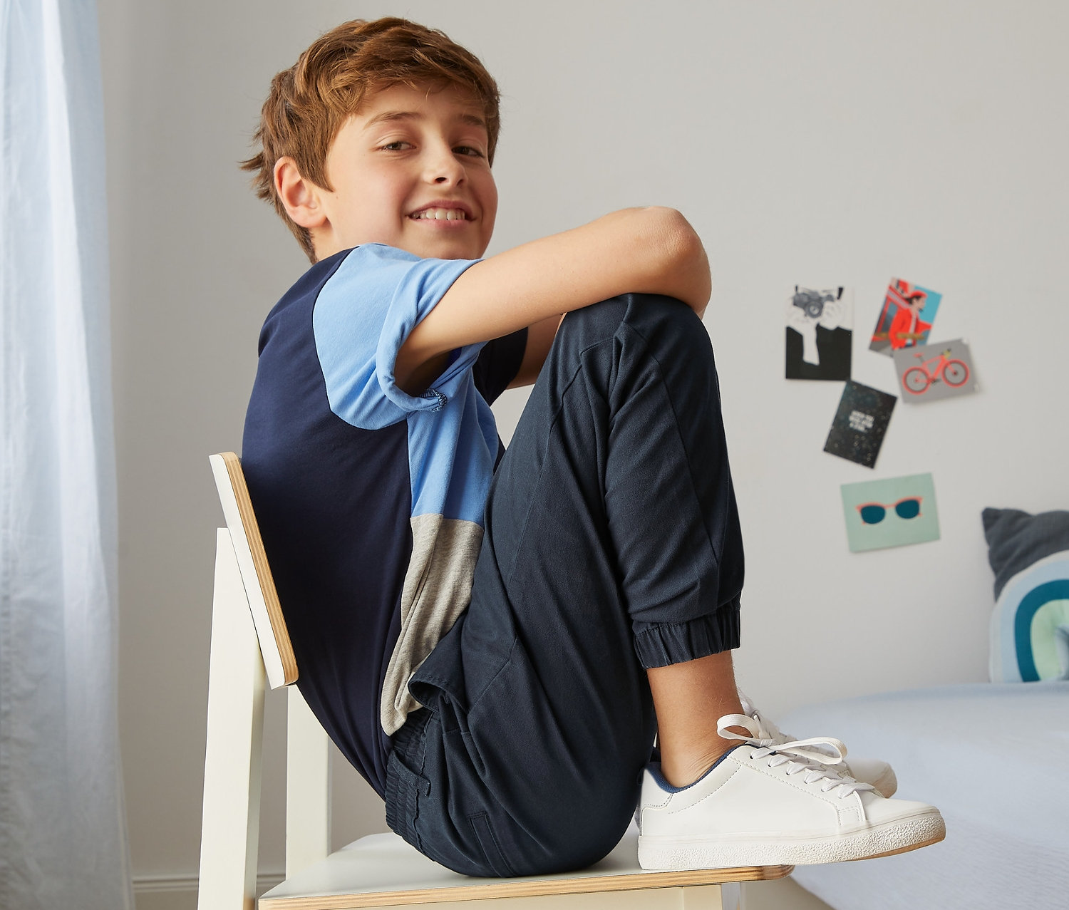Chlapec sedí na židli v tmavě modrých chino kalhotách v joggingovém stylu.