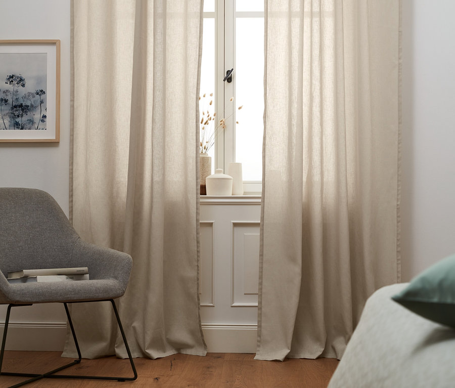 Béžové pololněné závěsy zakrývají okno.