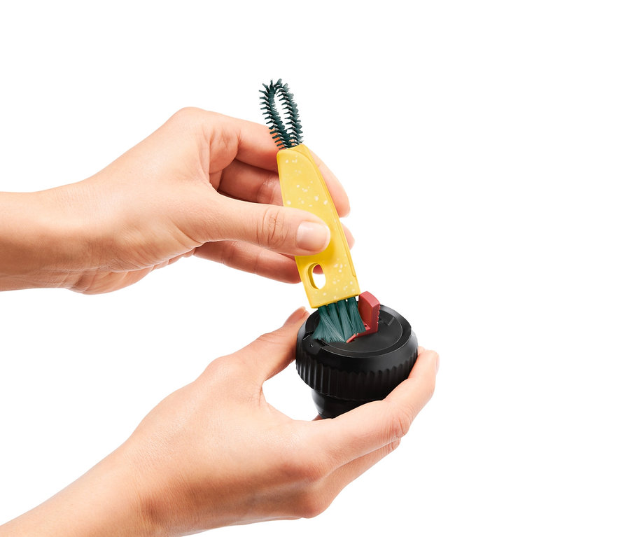 Ruce čistí černý spotřebič pomocí žlutého multifunkčního kartáče 3 v 1.