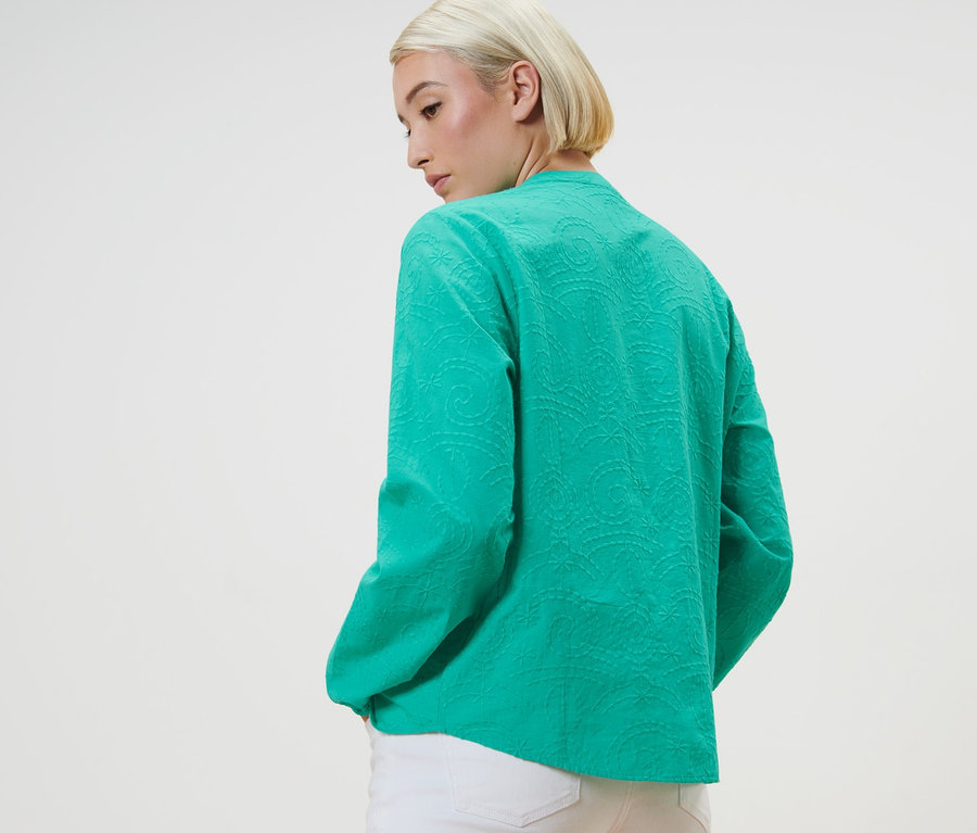 Žena pózuje v zelené halence s výšivkou.