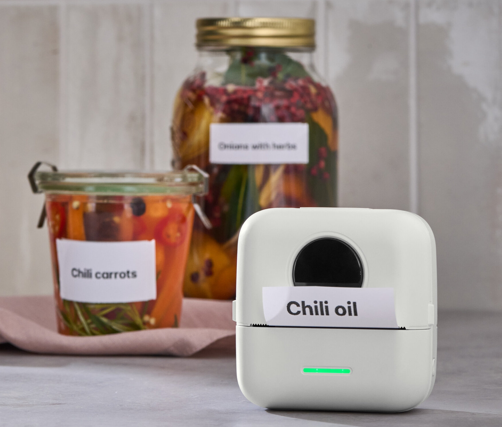 Mini termotiskárna vytiskla štítek s nápisem Chilli oil. V pozadí sklenice s chilli mrkví.