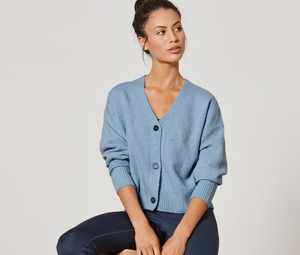 Žena sedí na stoličce a má na sobě modrý kardigan z hrubé pleteniny.