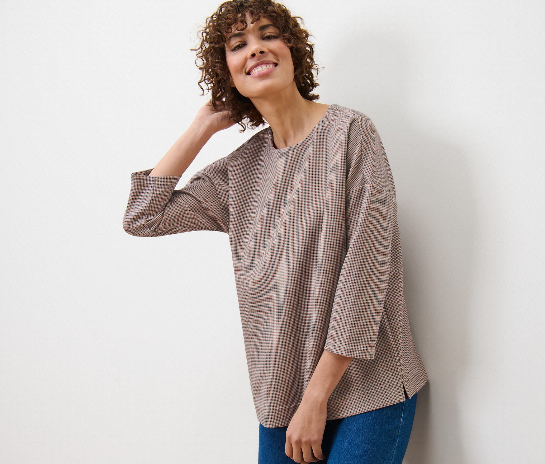 Žena se opírá o stěnu a má na sobě kostkovanou mikinu a džíny.