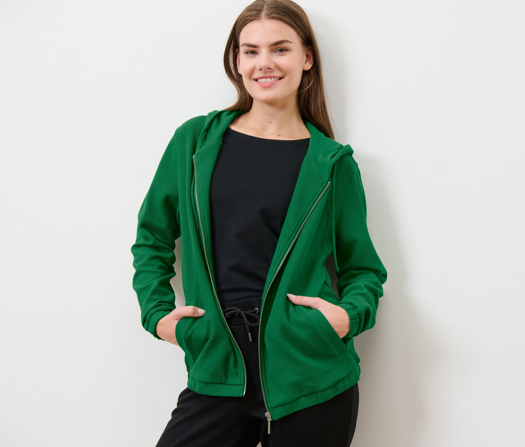 Žena pózuje v zelené mikině.
