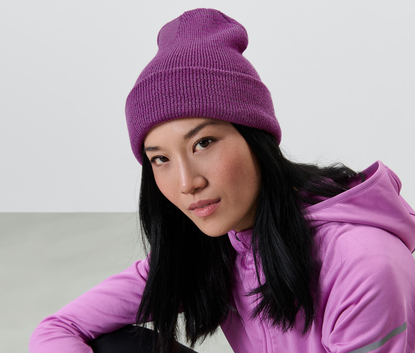 Asiatka s dlouhými černými vlasy má na sobě fialovou pletenou čepici a fialovou mikinu s kapucí.