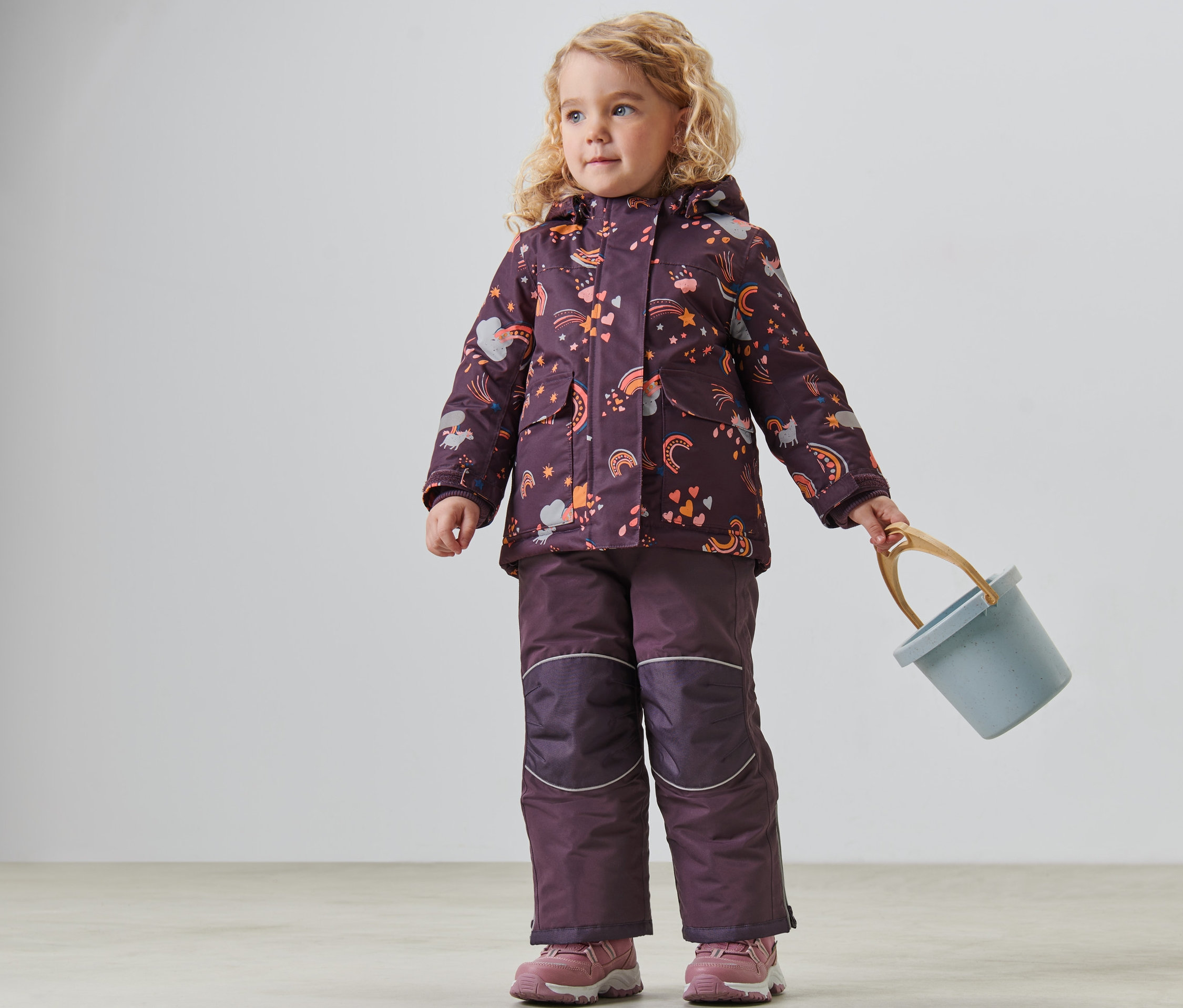 Holčička v dětské zimní kombinéze drží modrý kyblík.