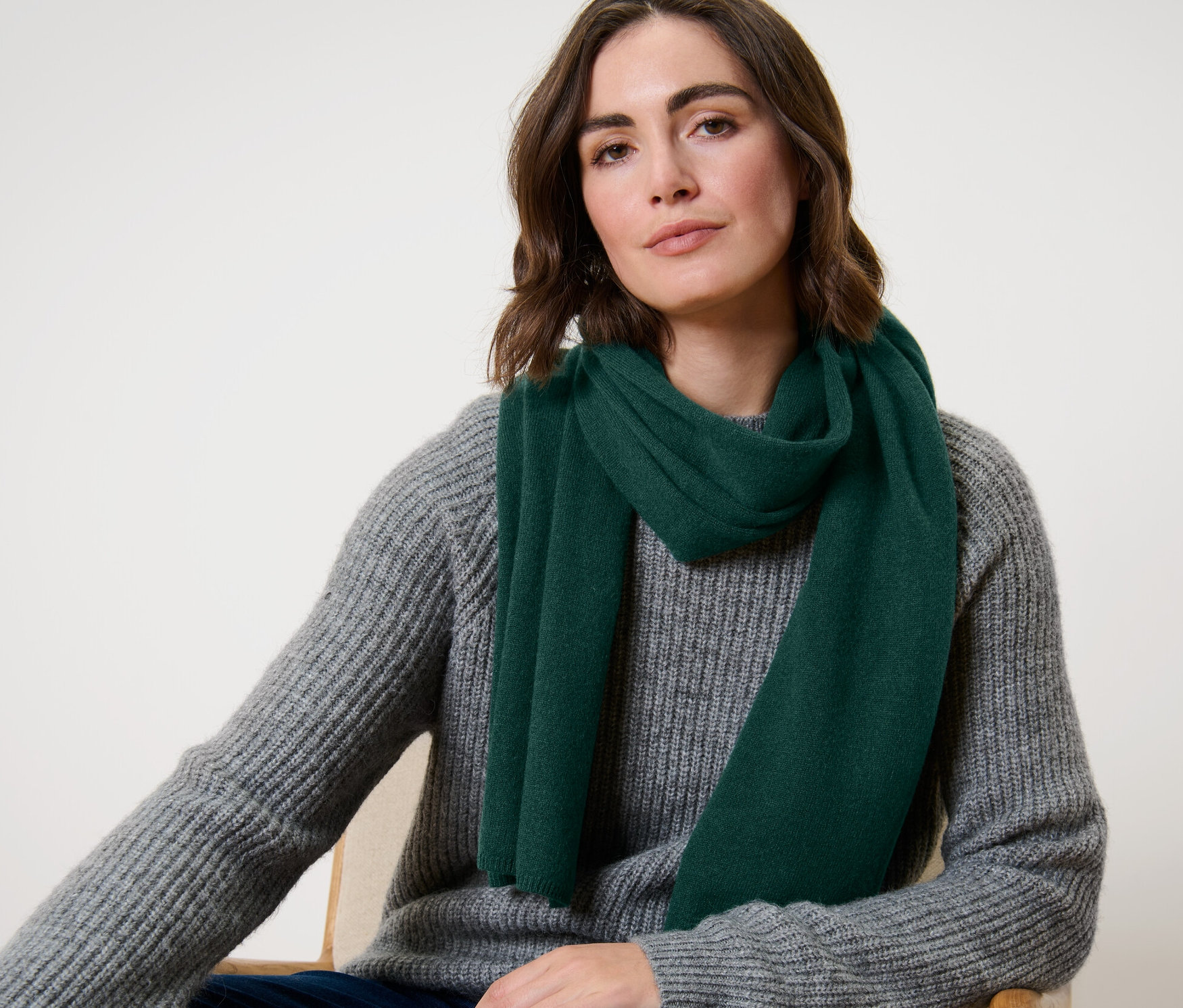 Žena sedí a má na sobě tmavě zelenou kašmírovou pletenou šálu.