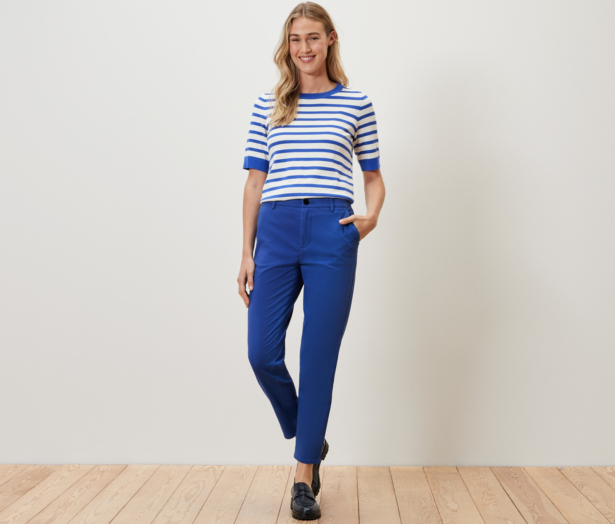 Žena pózuje v kobaltově modrých chino kalhotách a pruhovaném topu.